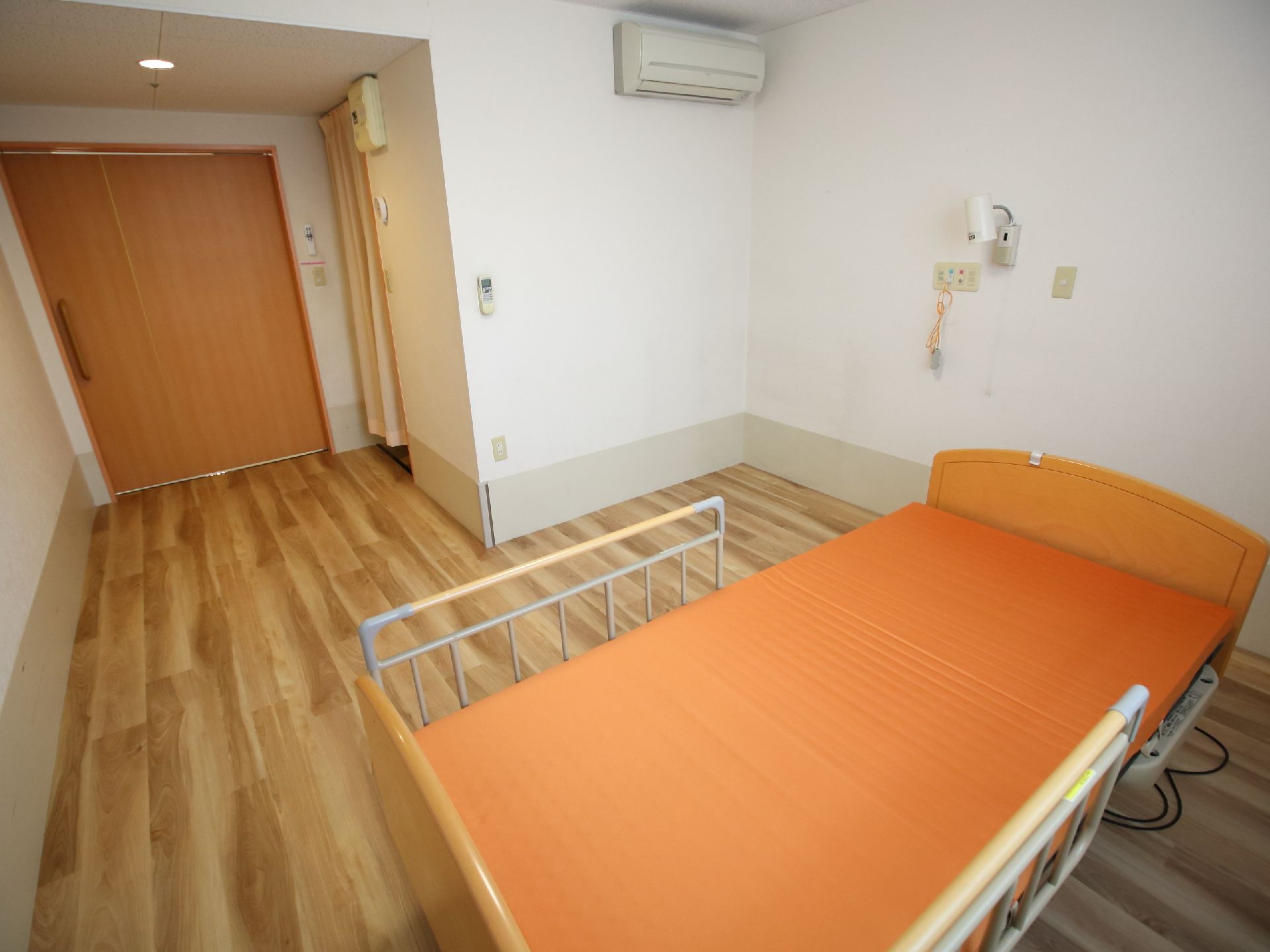電動式の介護用ベッドが用意された、濃い木目のフローリングを敷いた部屋