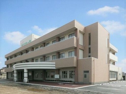 どっしりとしたベージュの３階建ての建物。各フロアにベランダが付き、外壁にはホーム名が書かれている。