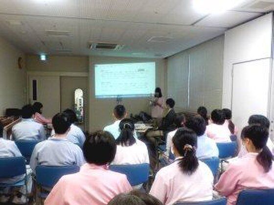 大勢のスタッフが研修を受けている様子。みないすに座り、前のスクリーンに映し出された画像を見ている。