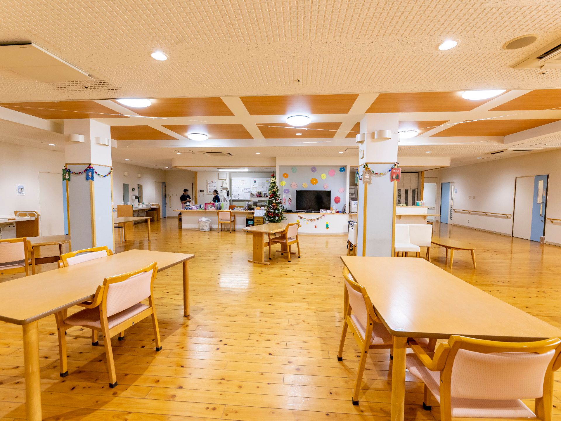 エアコンが付いたシンプルな居室。寝具付きのベッドや肘置きが付いた一人用の椅子が置かれ、ワイドタイプの洗面所が設置されている。