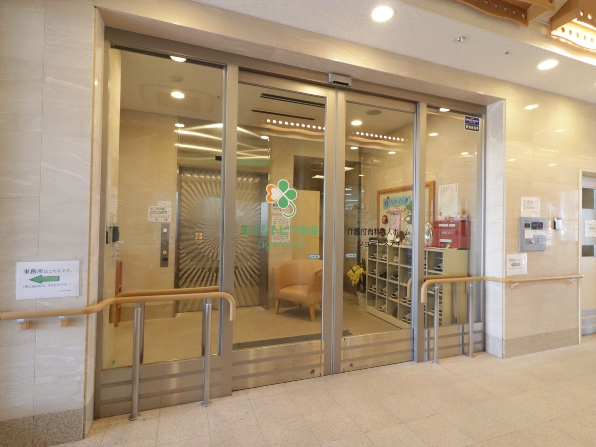 横幅のあるガラス張りの自動ドアである。横の壁にはインターホンが取り付けられており、両サイドには手すりが設置されてる。