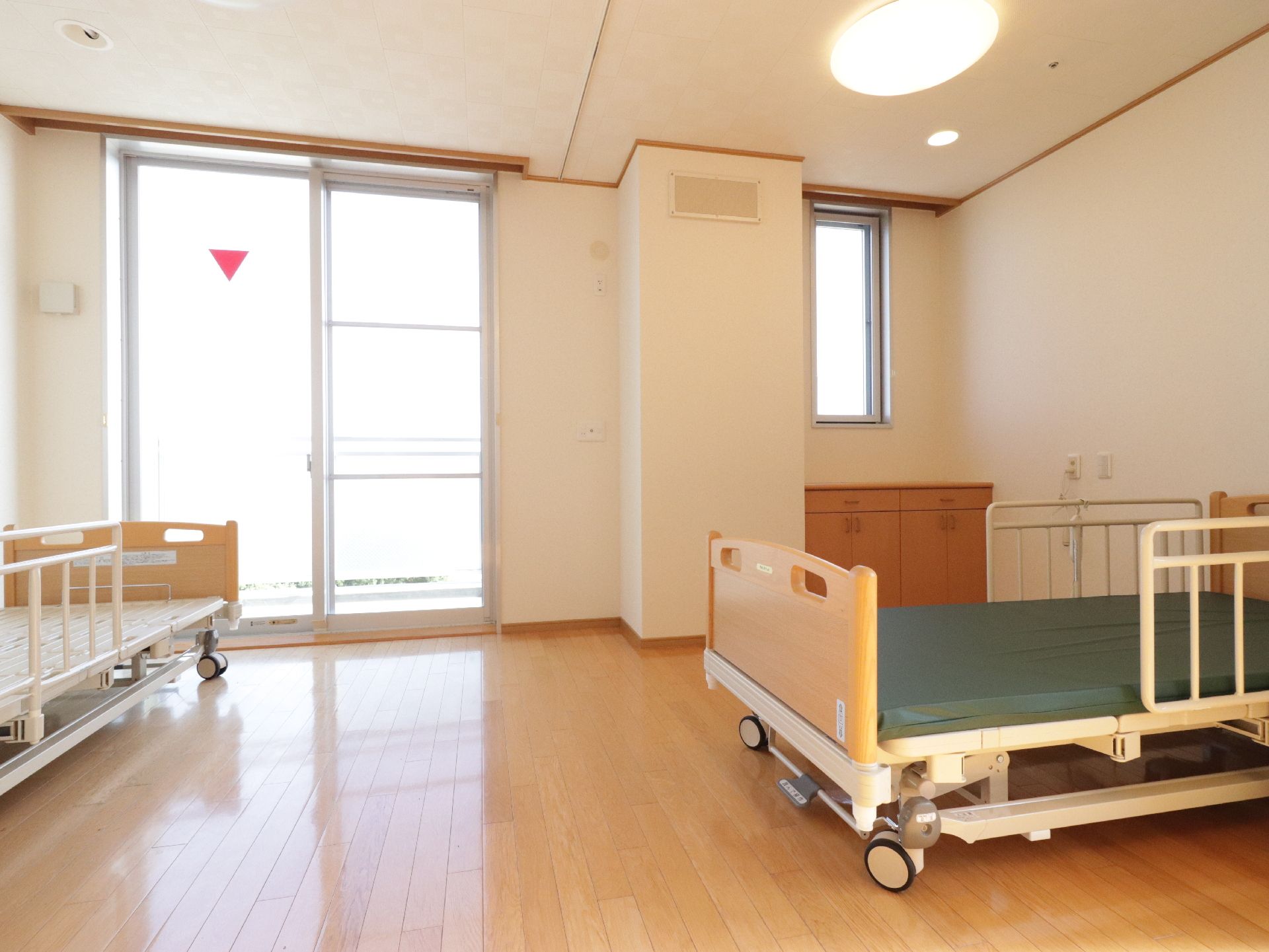 キャスター付きの介護用ベッドが複数置かれた、フローリングの部屋