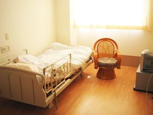 ベッドや小さないす、テレビ台などが置いてある施設内の個室の様子