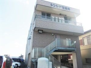 鉄骨造の建物の写真。手前に駐車場スペースがある様子。天気が良い日の１枚