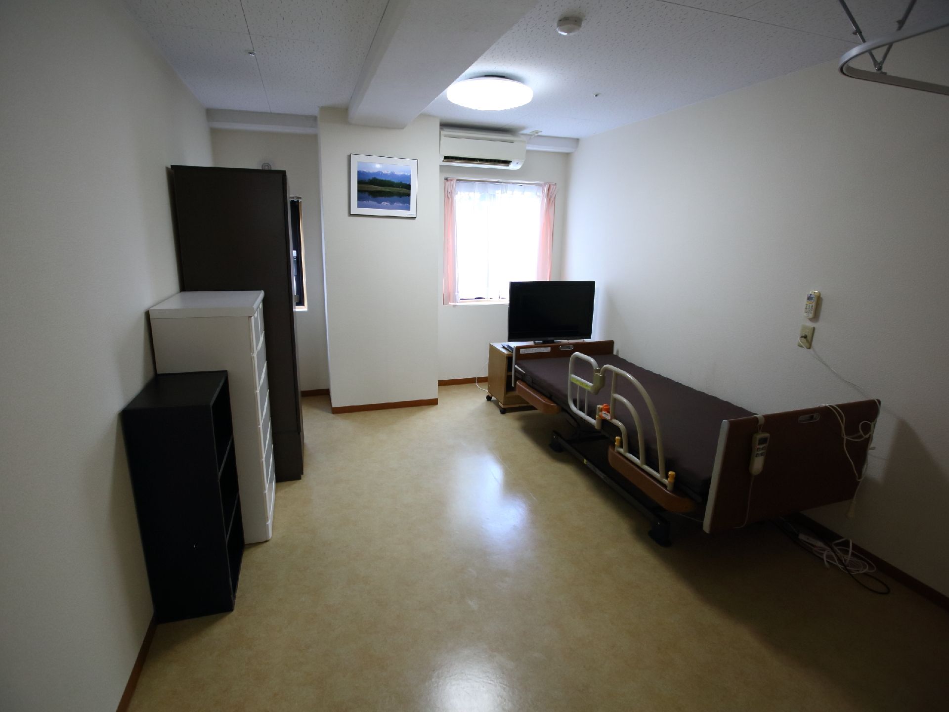 介護用ベッドのほか、テレビや複数の収納を備えた、樹脂製の床材を張った部屋