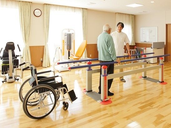 車いすの男性が平行棒を使用した訓練を実施中。平行棒横には白い上着を着たスタッフがいる。