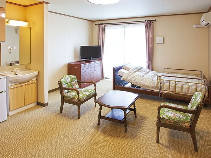 備え付けの洗面所が左手にあり、応接セットやテレビ、収納、ベッドなどが置かれた居室。