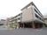 ベージュと白を基調とした外壁の大きな建物である。まわりは広々としており、横には駐車場や横断歩道がある。