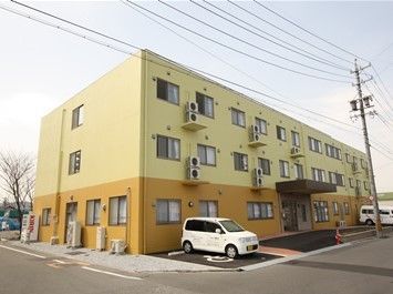 長方形の建物の中央に入口がある。入口前には、屋根が張り出した構造をしている。建物の前面に駐車場を完備している。
