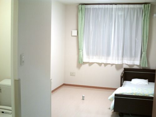 個室の居室はバリアフリーになっており、トイレや介護ベッドが完備されている。カーテンが掛かっている窓がある。