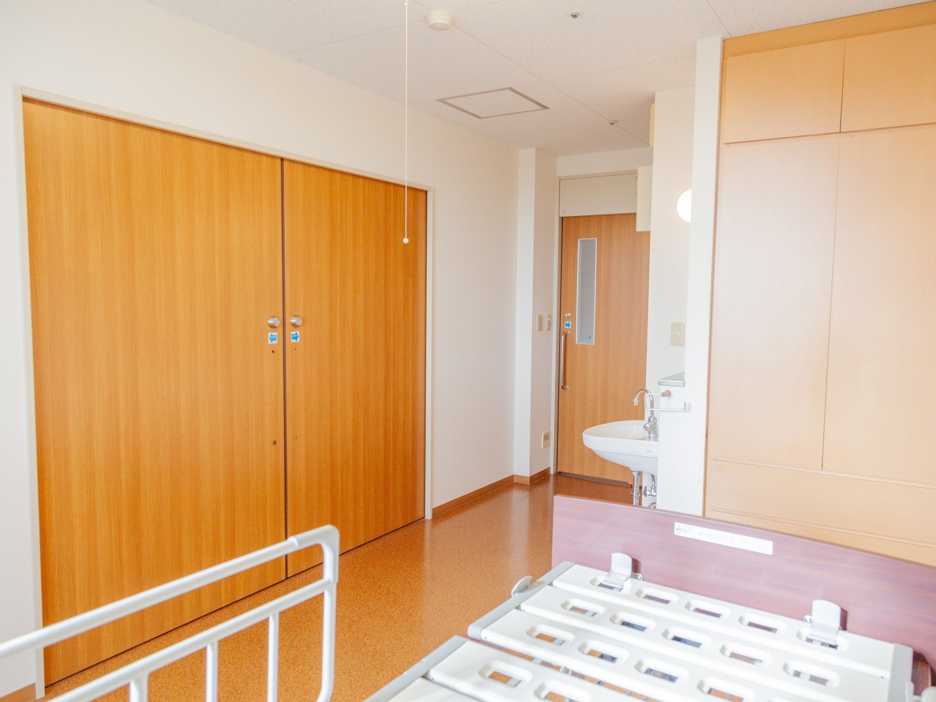 淡い色のカーテンをかけ、エアコンと介護用ベッドを備えた、白い壁紙の居室