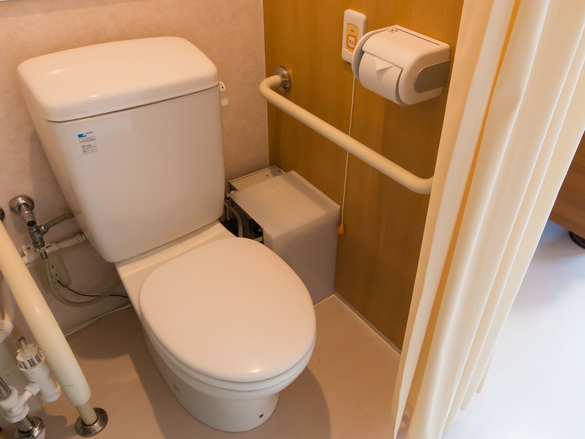 個室に設置されたトイレには、呼び出しボタンや手すりが完備されている。緊急時に対応しやすいように、カーテンで仕切るようになっている。