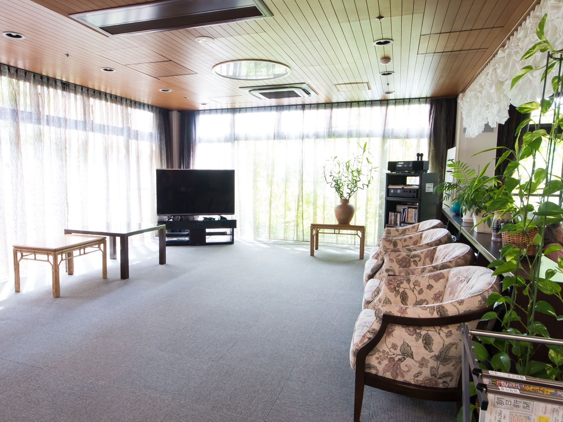 ホールは２方面に窓があり、日当たりが良く広々としている。レクリエーションができるように、テレビやカラオケ機器が置かれている。