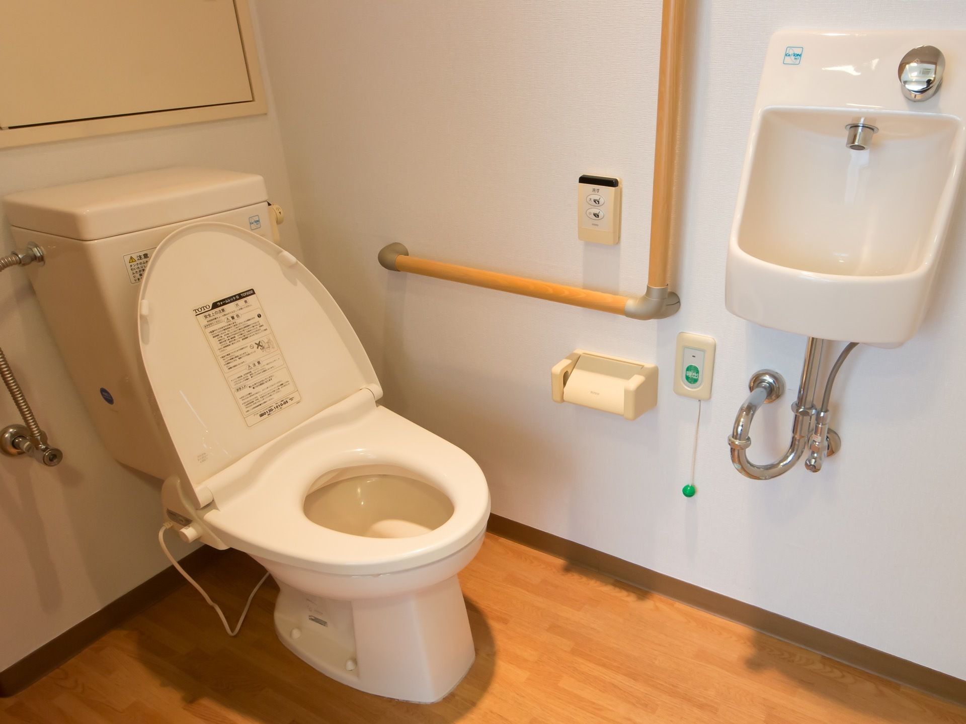 トイレには手すりが取り付けられている。手洗い場が設けられている。壁にトイレットペーパーホルダーが設置されている。