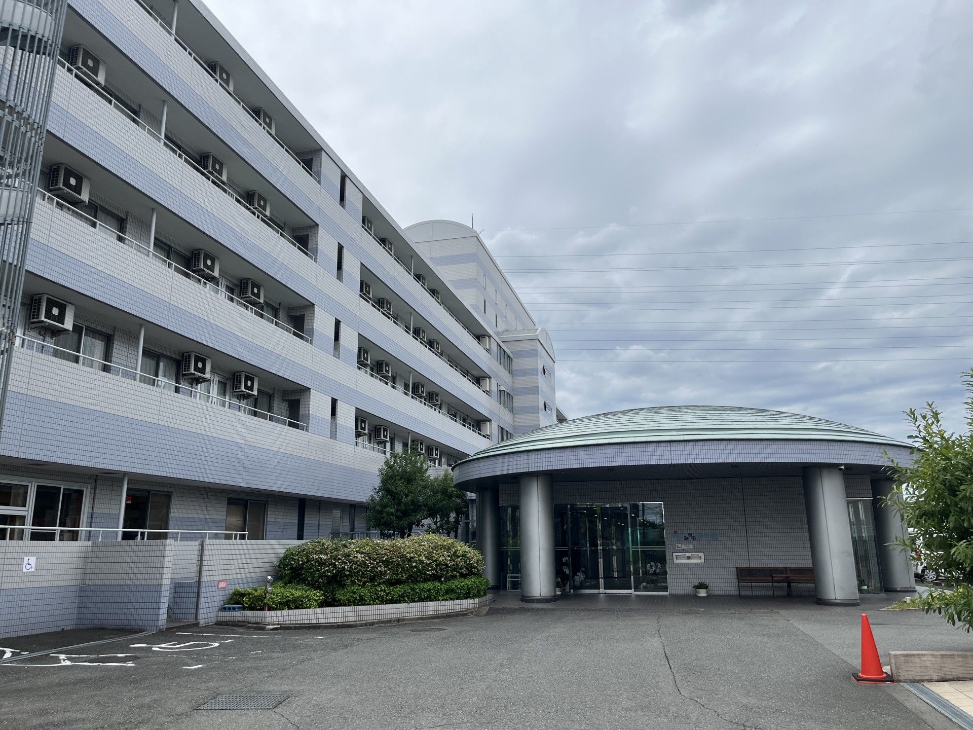 白とライトブルーの大きな建物の前には駐車場があり、側面には屋外階段も付いている。