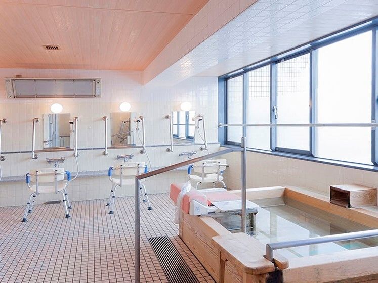 手すりが鏡の両サイドに付いたシャワスペースが奥にあり、手前にはヒノキでできた浴槽が置かれている。