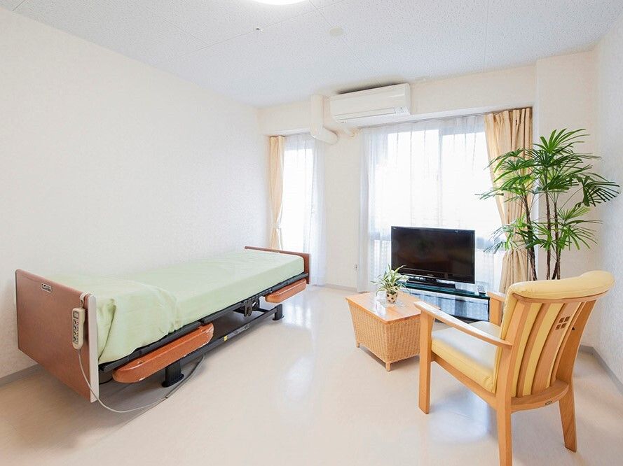 寝具付きのベッドがあり、エアコンやテレビ、一人用の椅子が設置された部屋。大きな窓も付いている。