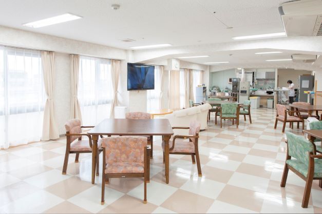 ピンクやグリーンの椅子がセットされた木製のテーブルが複数置かれたスペースにはテレビもある。