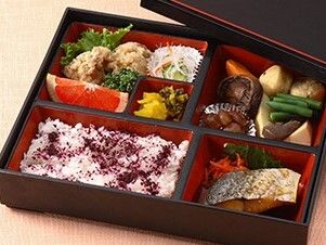 弁当風の入れ物に煮しめや焼き魚、カットフルーツ、酢の物、漬物、ゆかりご飯などが詰められている。