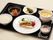 黒いお盆に白身魚のムニエルとコーンスープ、野菜、白いご飯が載せられている。