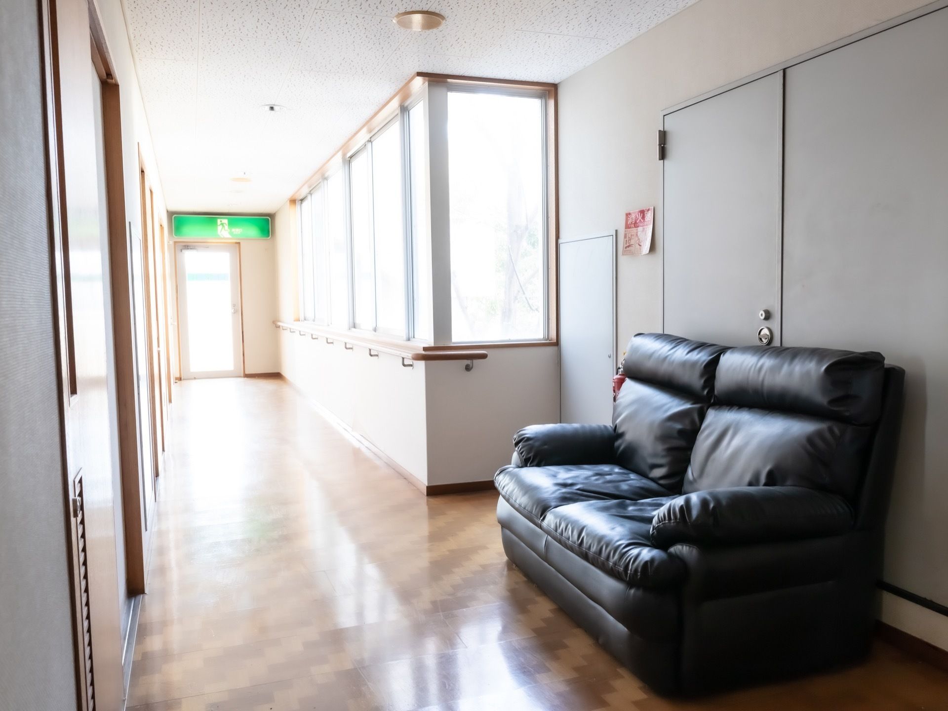 幅が広い通路の奥の壁に、避難口誘導灯が設置されている。ブラックカラーの２人掛けのソファが置かれている。