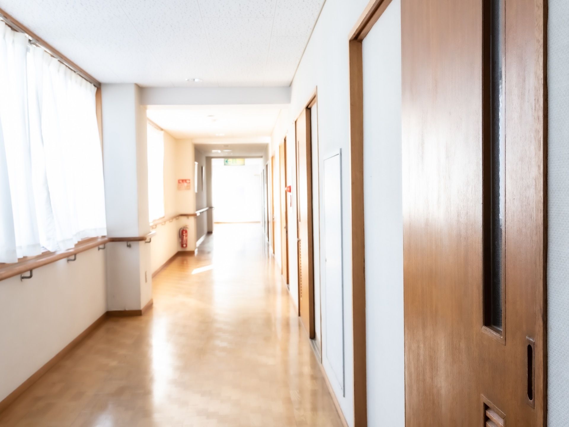 陽の光が良く差し込んでいる明るい通路が直線にある。片側に居室が並んでいて、反対側は一面窓。壁には手すりが付いている。