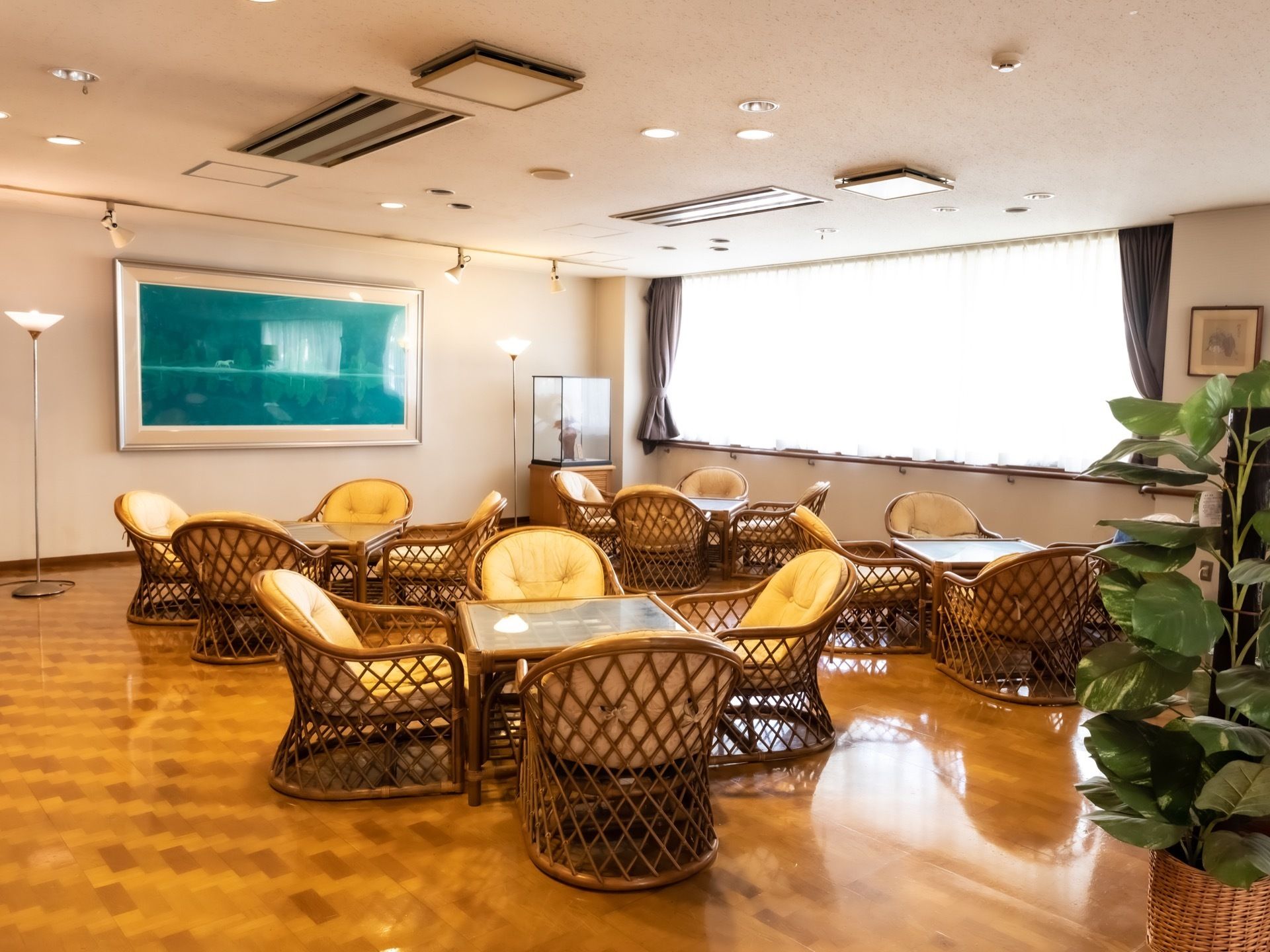 明るい部屋に籐のテーブルと椅子がある。窓からは陽が差し込み、壁には大きな絵が掛けてある。観葉植物も置いてある。