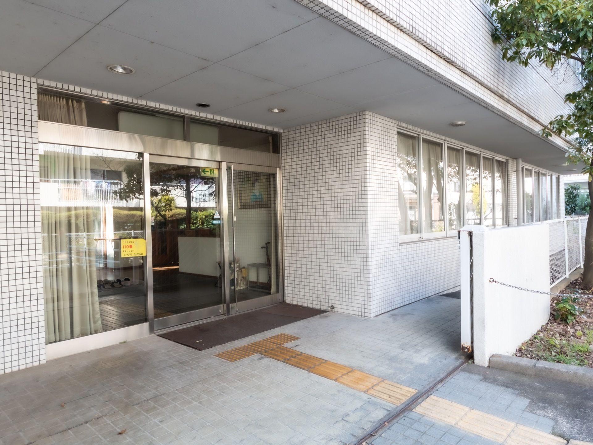 玄関扉は全面ガラスの自動ドアになっている。外壁は白いタイル状になっている。玄関上にはスポットライトが付いている。