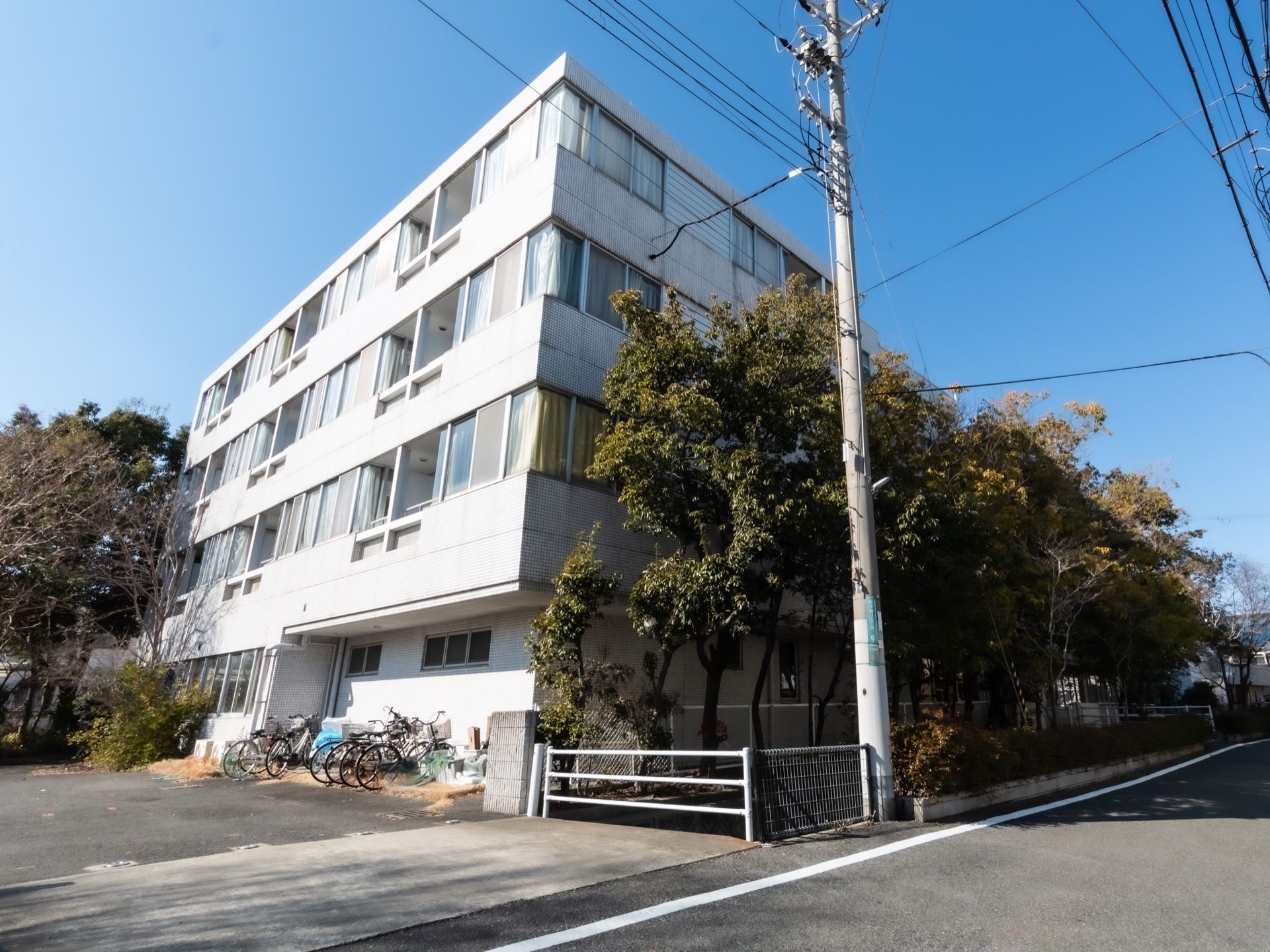 4階建ての施設の外観は白を基調としていて、居室の窓が大きくなっている。周りには木々があり、敷地内入口も広い。