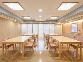 長方形のテーブルが4つ並び、それぞれに椅子がセットされている。部屋の奥には大きな窓がある。