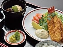 黒い盆に乗った食事。エビフライやサラダを主催として、吸い物や漬物が置かれている。