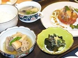 煮物にスープ、わかめのおひたし、洋風のメインと、和洋折衷の食事。白いご飯もある。