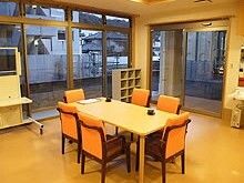 大きな窓があり、6人掛けのテーブルが置かれている。出入り口には自動ドアがあり、靴箱も設置されている。