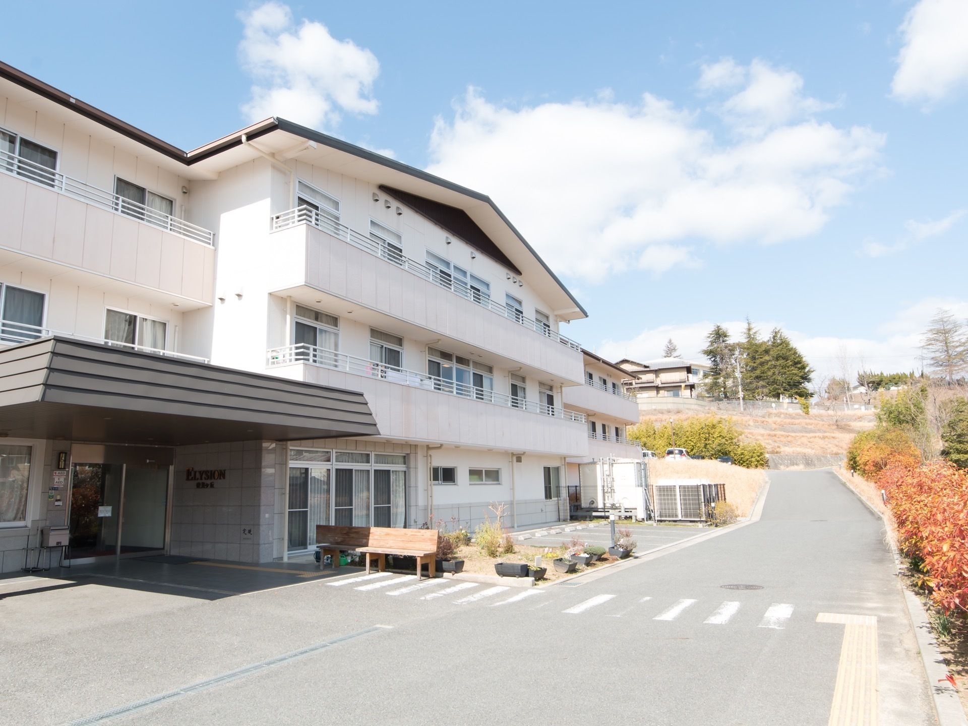 車道に面して施設が建てられている。車道と敷地内との間に段差は無く、建物の正面に横断歩道があるので、徒歩や車椅子でも往来しやすい。