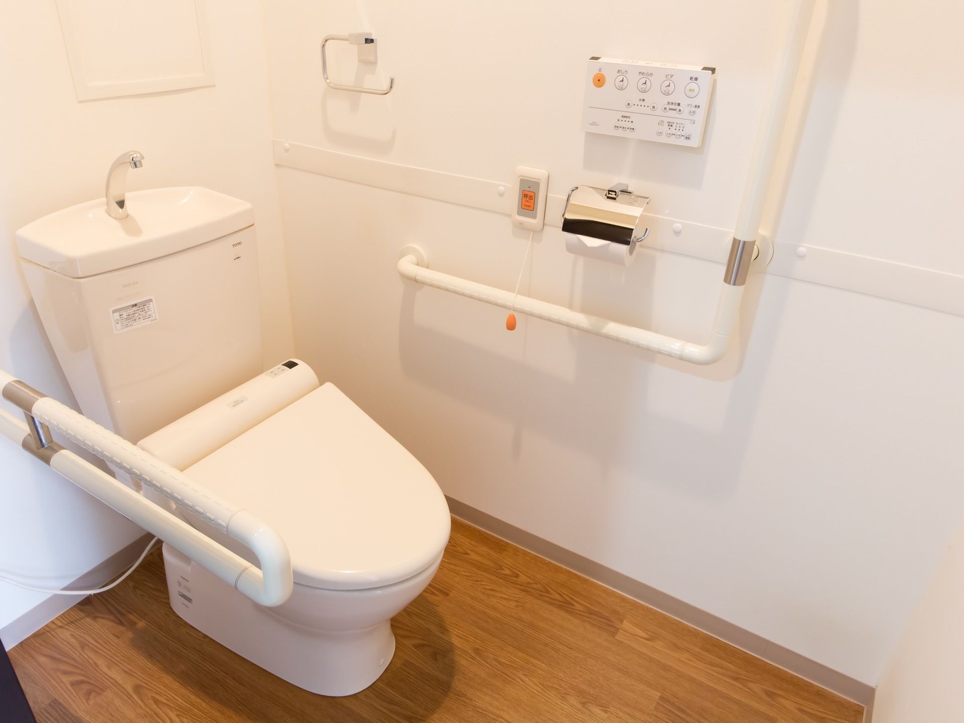 トイレは白色で統一され、明るく清潔感がある。壁には温水洗浄機能の操作パネル、緊急用のボタンが取り付けられている。