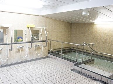 白いタイルが貼られた浴室には大きなの浴槽と複数のシャワーがあり、手すりも設置されている。