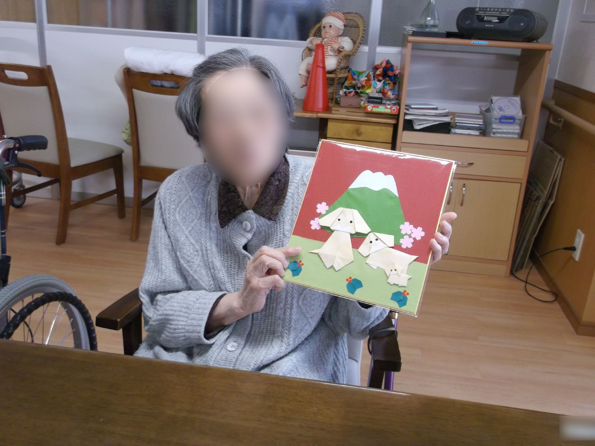 工作の作品を両手でもってカメラに向かって微笑む入居差。