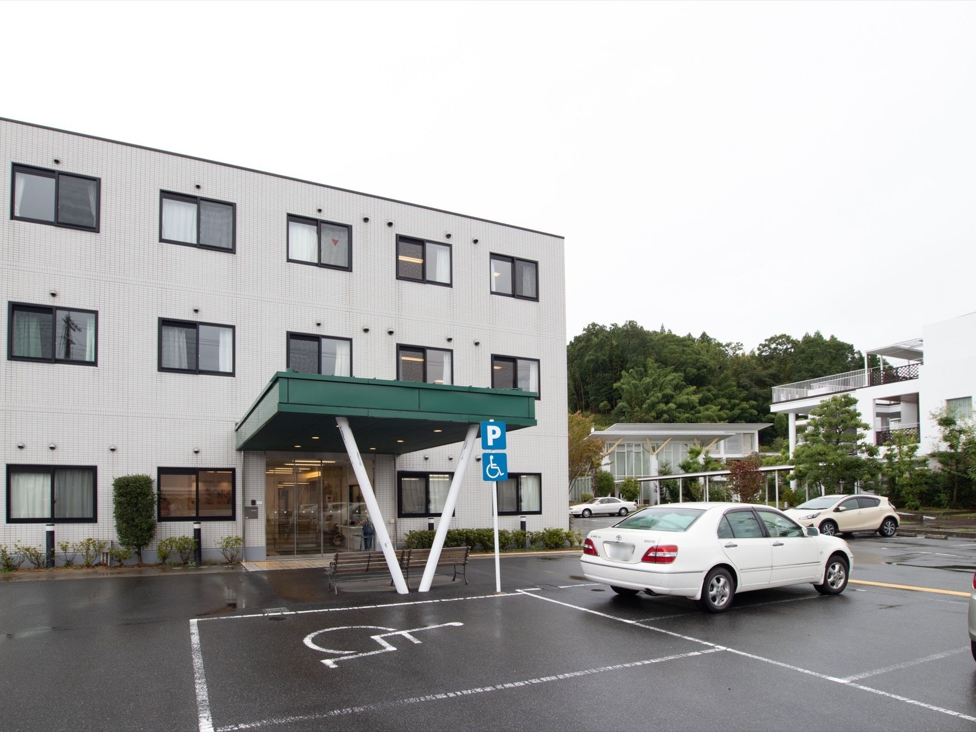 三階建ての建物である。玄関にはひさしが設けられており、その下にはベンチが用意されている。前方には駐車場がある。