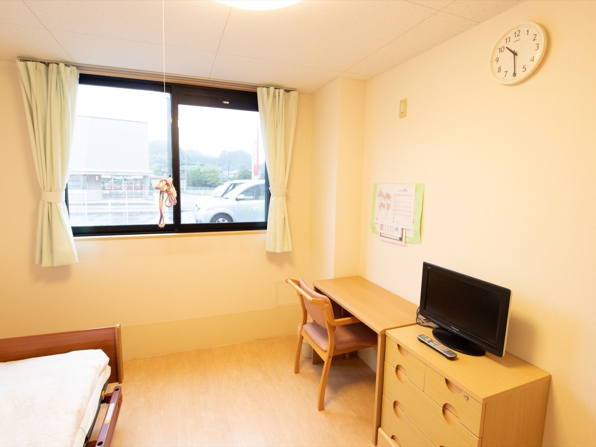 机と椅子がセットで用意されている。収納の上にはテレビが置かれている。窓の外には広い駐車スペースがある。