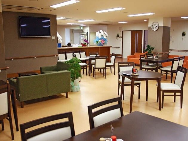 サイズの異なるテーブルセットが複数置かれている食堂。グリーンのソファの前にはテレビもある。