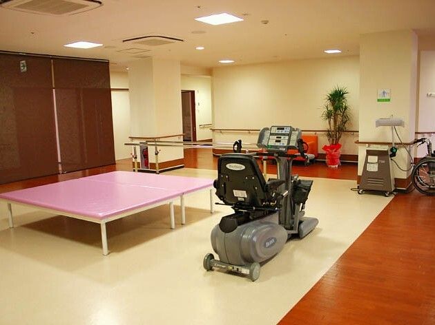 平行棒やリハビリ用のベッド、サイクリングマシンなどがそろったスペース。観葉植物も飾られている。