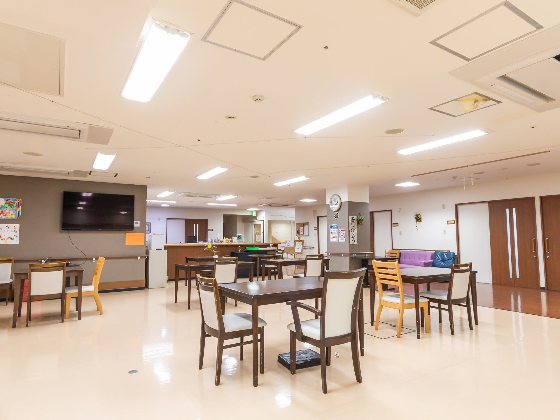 様々なデザインのテーブルセットが複数置かれている食堂。テレビの前にはソファも置かれている。