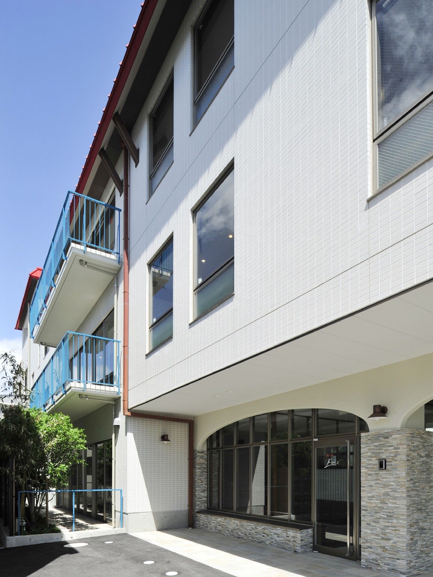 ベージュの2階建ての建物には屋外階段が付き、広い駐車場もある。門には赤い文字でホーム名が書かれている。
