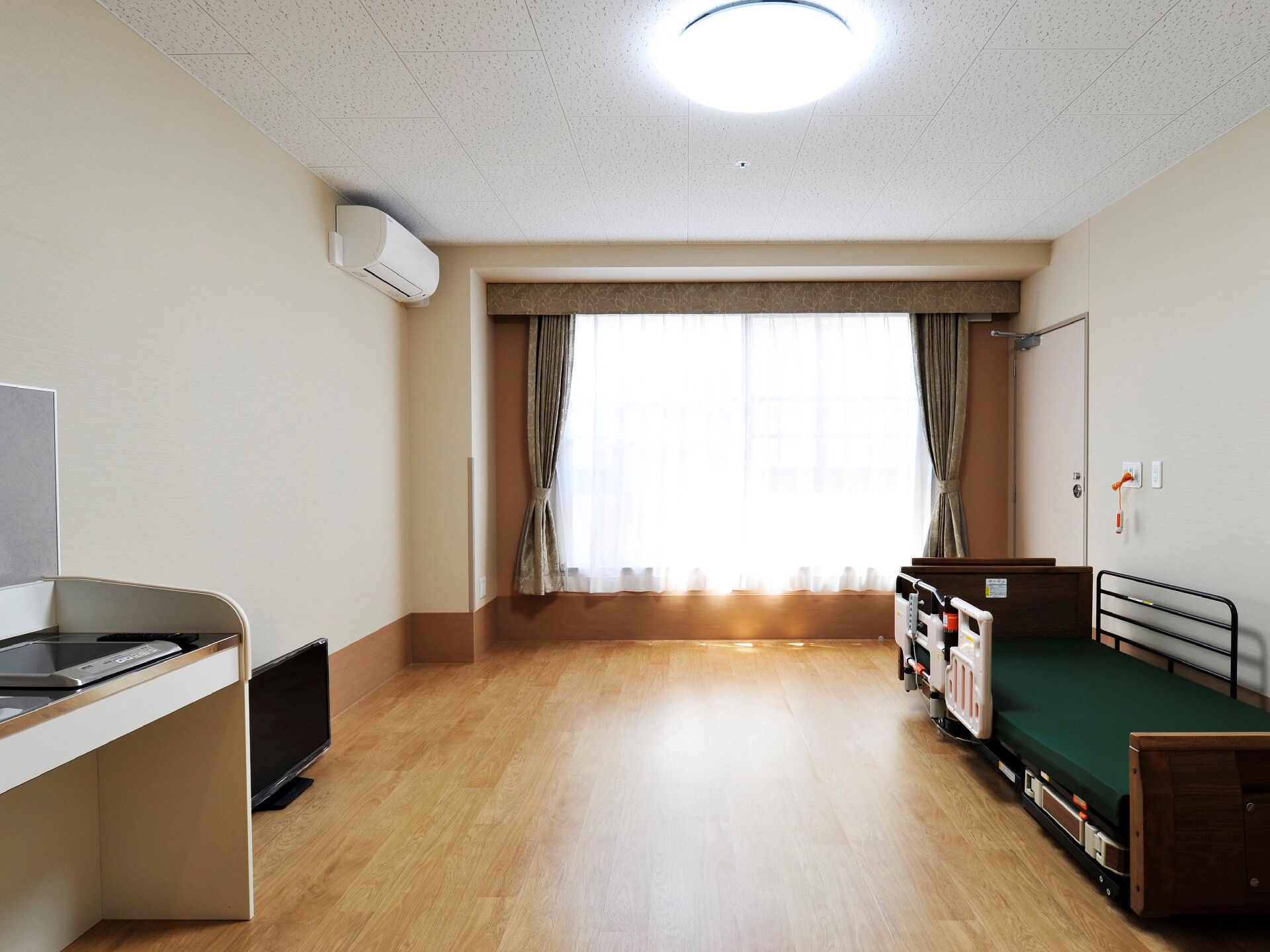 エアコンが付いたフローリングの居室。寝具付きのベッドやタンス、テレビもあり、日当たり良好。