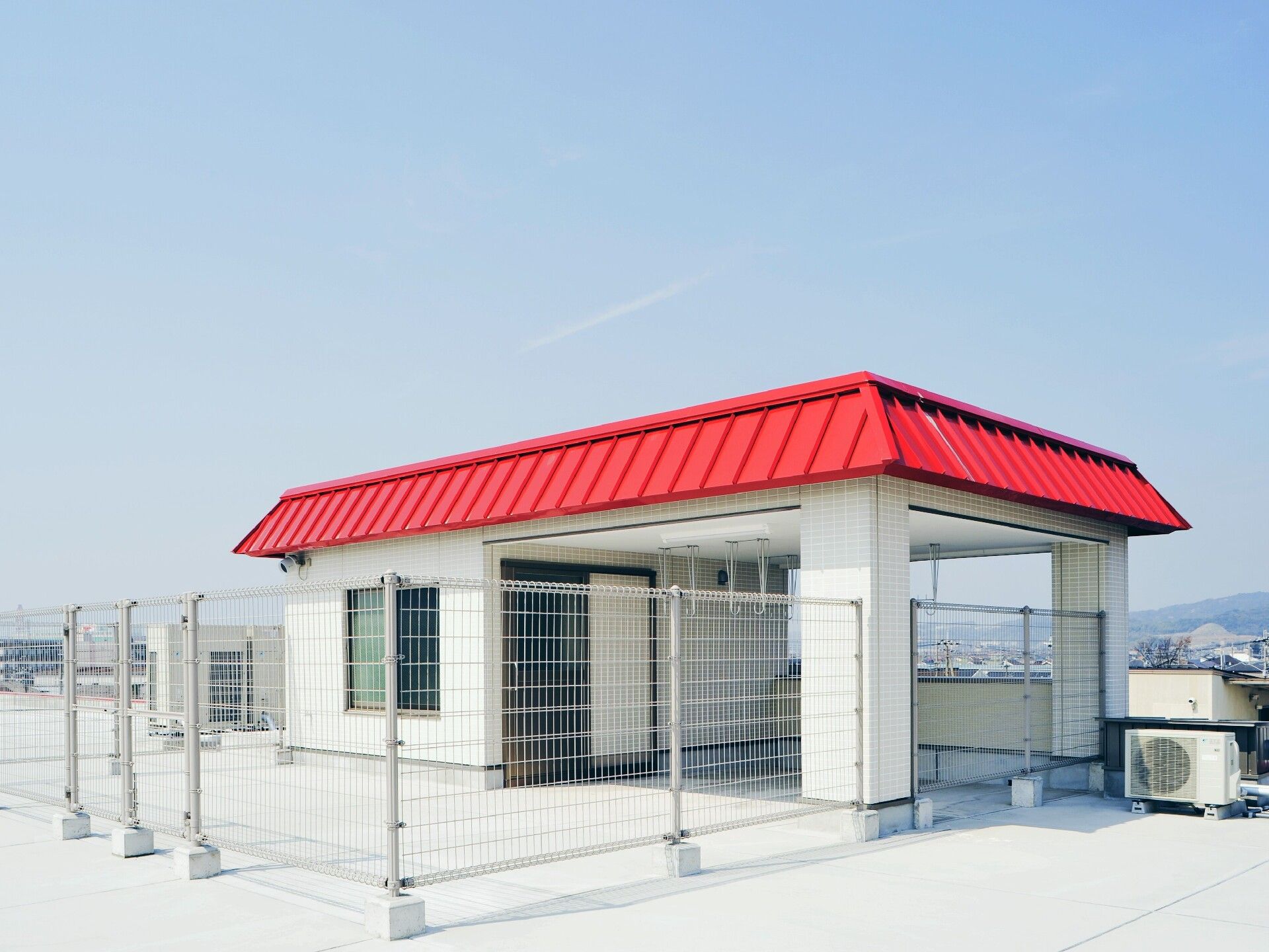木製のベンチが複数設置された広い屋上。周辺には住宅地があり、青い空が広がっている。