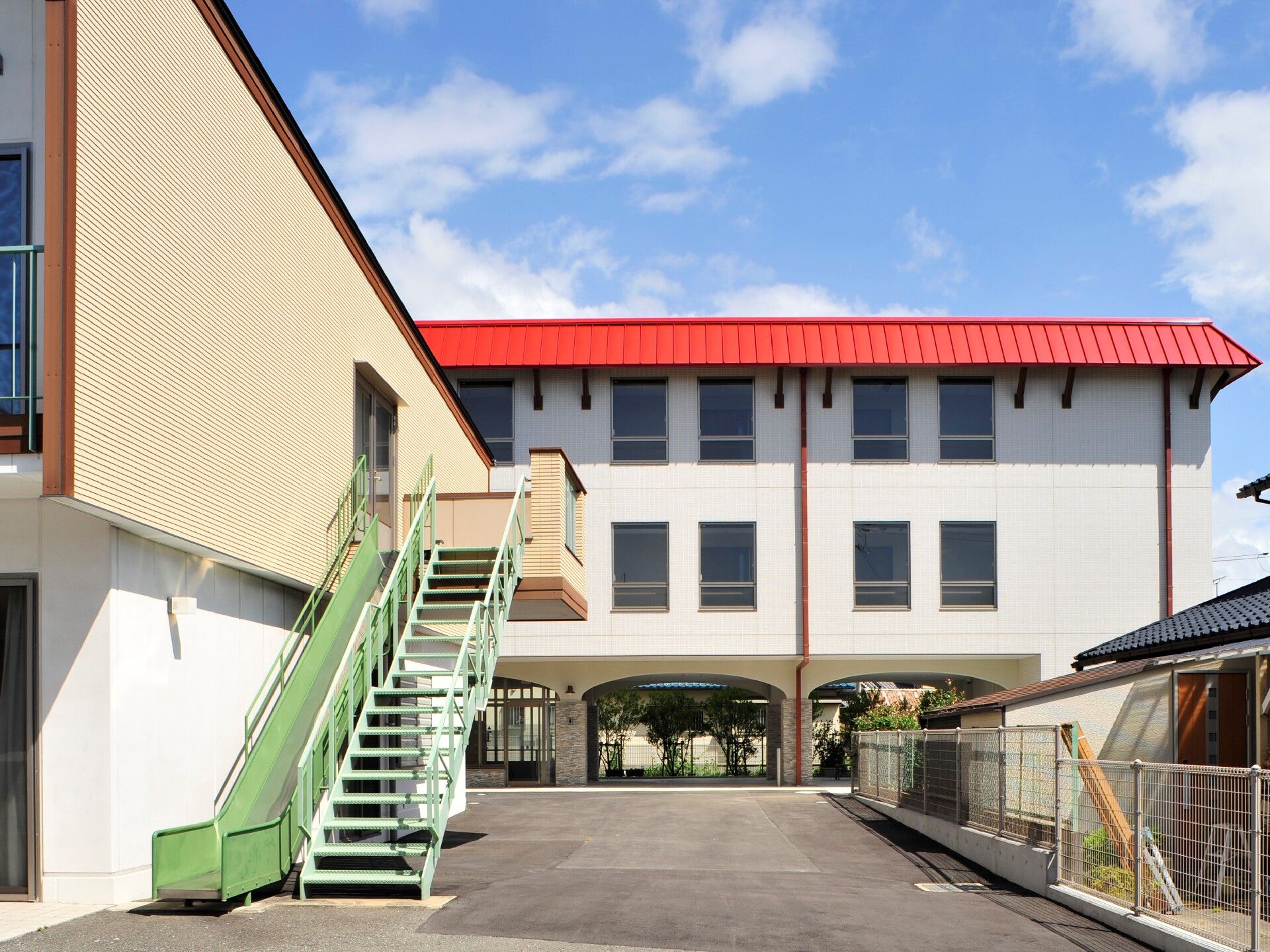 日当たりのいい場所にある2階建ての建物。敷地内には広い駐車場があり、建物の周辺には住宅地がある。