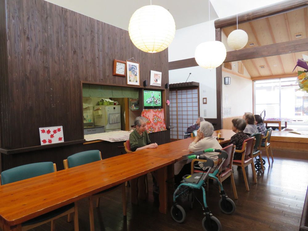 長いダイニングテーブルに6名の女性入居者が付き、テレビを見るなどして過ごしている。