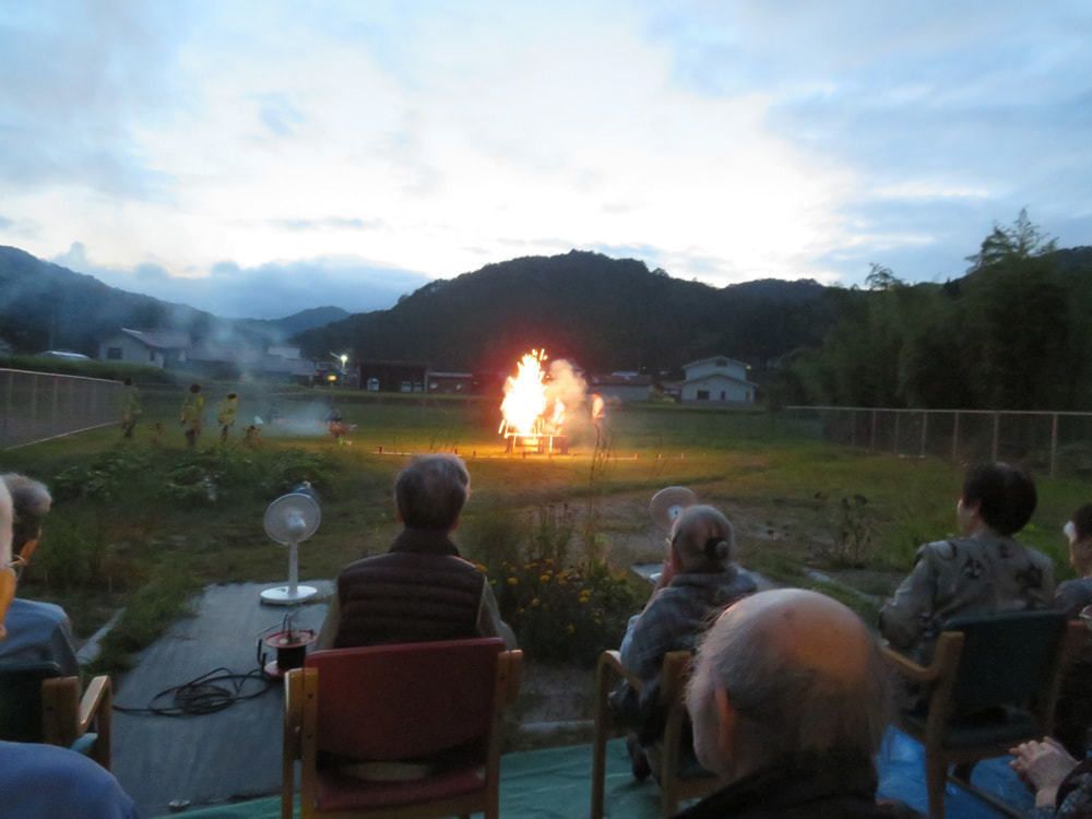 とんどの燃えている様子を椅子に座った入居者が眺めている様子。