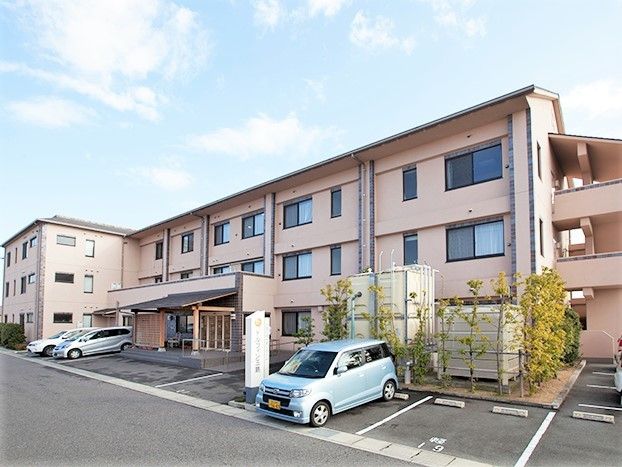 クリーム色の3階建ての建物は屋外階段もついていて、玄関周りには木や花が植えられている。