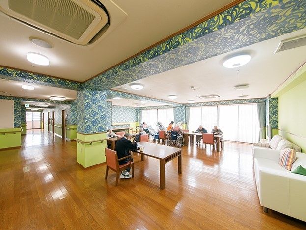 ダイニングテーブルが複数並び、思い思いの場所で入居者が過ごしている。